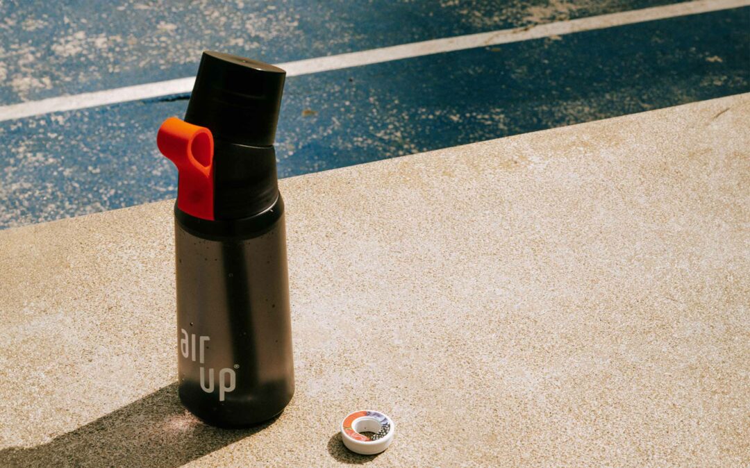 Black air up® scent-based water bottle with flavor pod, placed on concrete near a blue running track